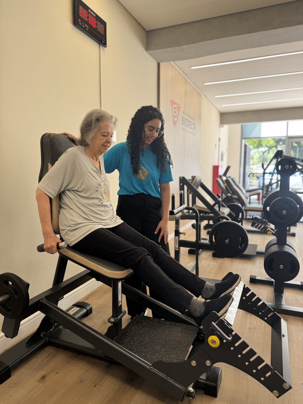A member using a calf machine at Studio Tekoá while a professional supports her from behind